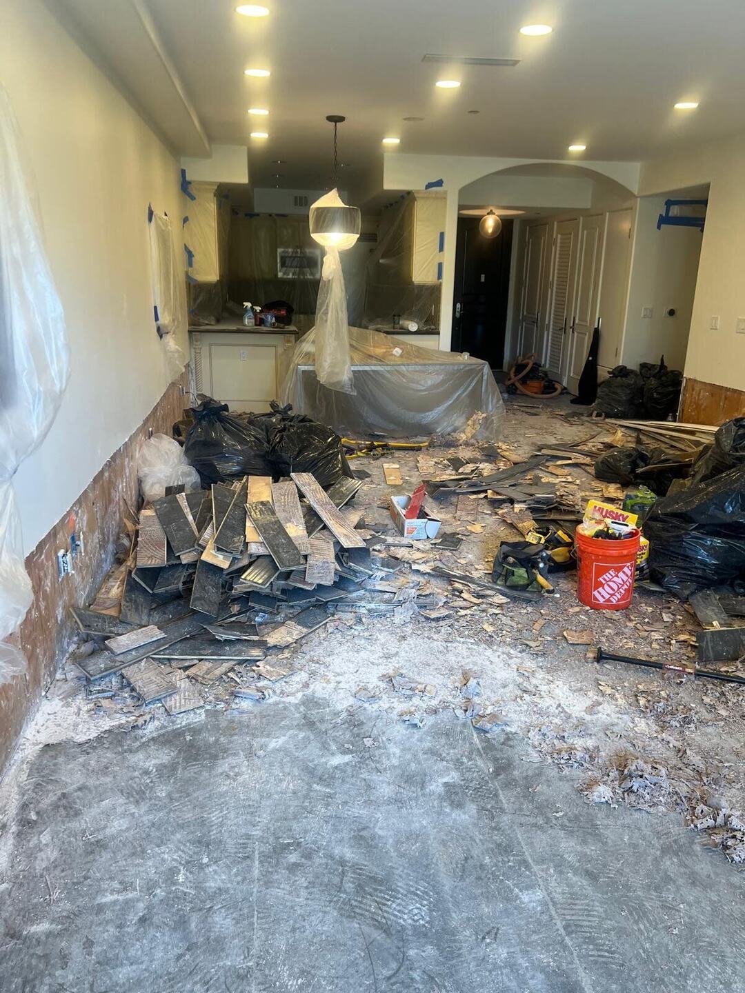 Flooring stripped to the concrete slab, debris bagged, kitchen wrapped